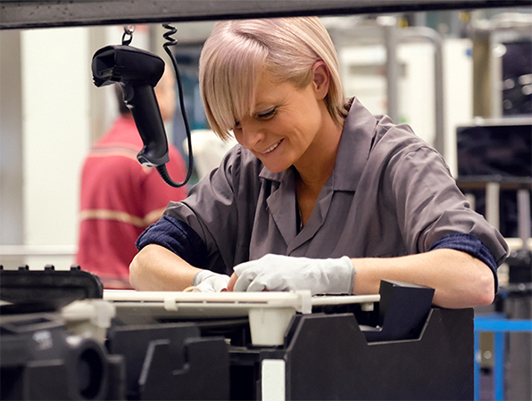 In an Apple manufacturing facility, two employees examine aluminum MacBook shells on titanium anodizing racks.